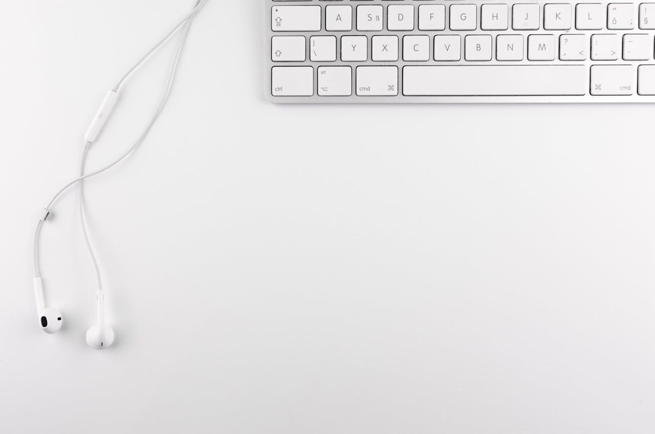 Top view of a minimal white desk setup featuring a keyboard and earphones on a clean background.